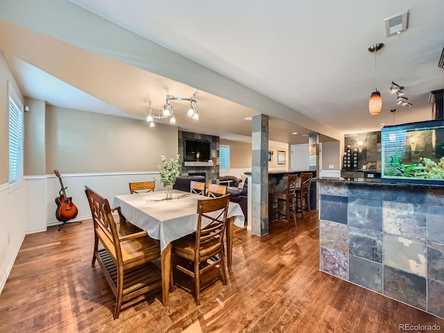 dining room featuring a tile fireplace, rail lighting, a dry bar, and wood finished floors