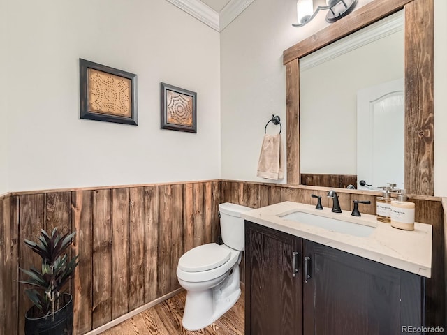 half bath featuring crown molding, vanity, wood finished floors, toilet, and a wainscoted wall