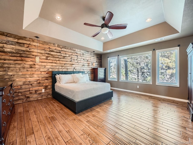 bedroom with ceiling fan, visible vents, a raised ceiling, baseboards, and light wood finished floors