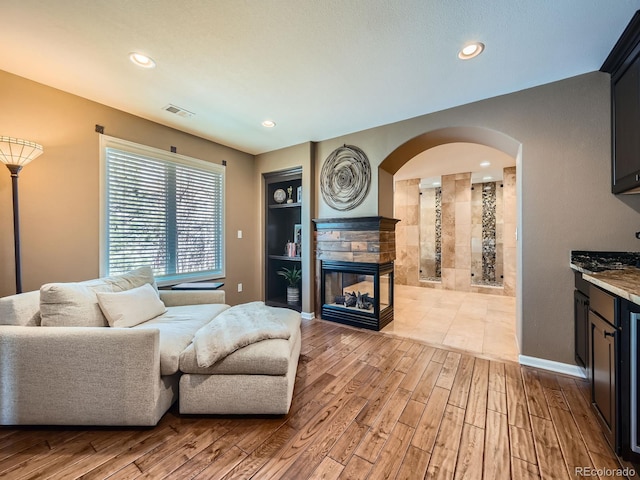 living room featuring light wood-style floors, arched walkways, a multi sided fireplace, recessed lighting, and visible vents