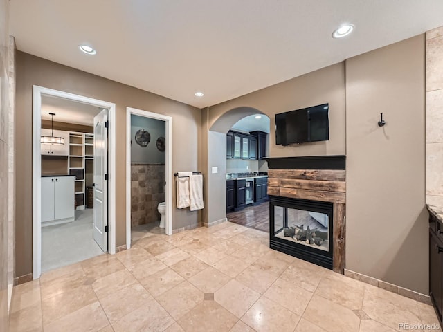 unfurnished living room with light tile patterned floors, arched walkways, tile walls, and a multi sided fireplace