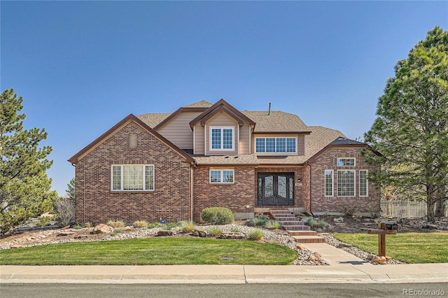 traditional-style house featuring french doors, roof with shingles, a front lawn, and brick siding