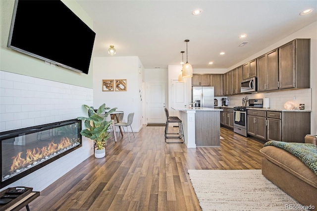 kitchen with a kitchen breakfast bar, hanging light fixtures, dark hardwood / wood-style floors, a kitchen island, and stainless steel appliances