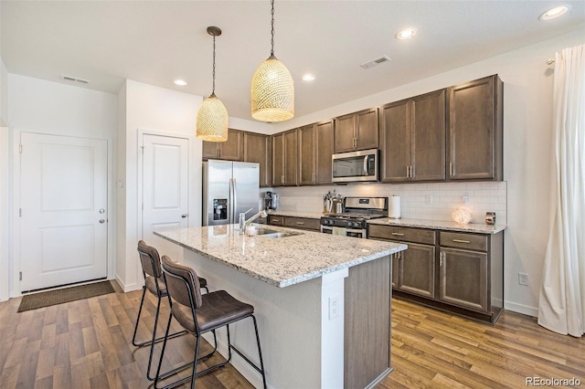 kitchen featuring light stone countertops, sink, decorative light fixtures, a center island with sink, and appliances with stainless steel finishes