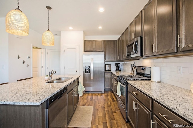 kitchen with tasteful backsplash, stainless steel appliances, sink, hanging light fixtures, and an island with sink