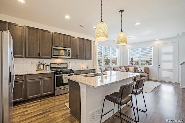 kitchen featuring light stone counters, stainless steel appliances, sink, pendant lighting, and an island with sink