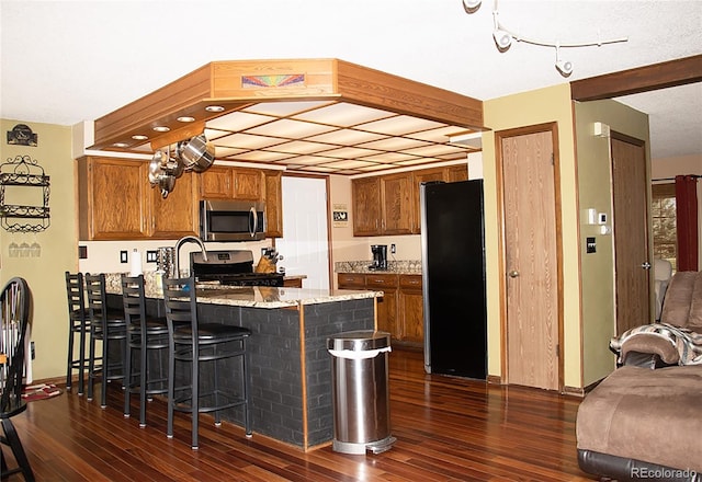 kitchen with black refrigerator, range, dark hardwood / wood-style floors, a breakfast bar area, and light stone counters