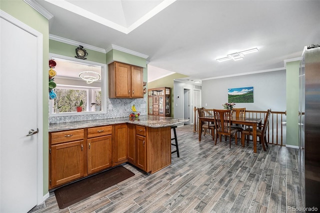 72 Rudi Ln W, Golden, CO 80403 - kitchen with wood finished floors, brown cabinets, a peninsula, backsplash, and ornamental molding