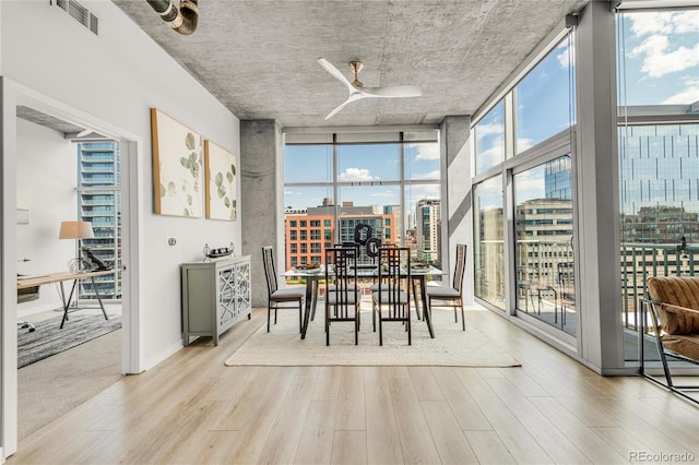 dining area featuring light wood finished floors, visible vents, floor to ceiling windows, a view of city, and a ceiling fan