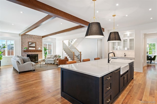 kitchen with light wood-type flooring, sink, white cabinetry, a brick fireplace, and decorative light fixtures