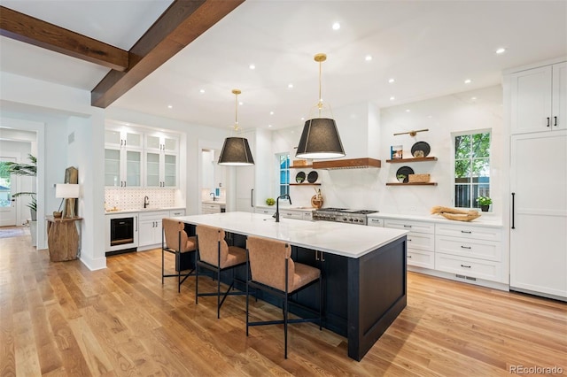 kitchen with beverage cooler, a center island with sink, white cabinetry, a breakfast bar area, and light wood-type flooring