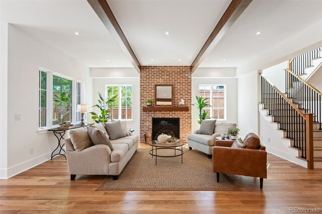 living room featuring light hardwood / wood-style floors, beamed ceiling, and a brick fireplace