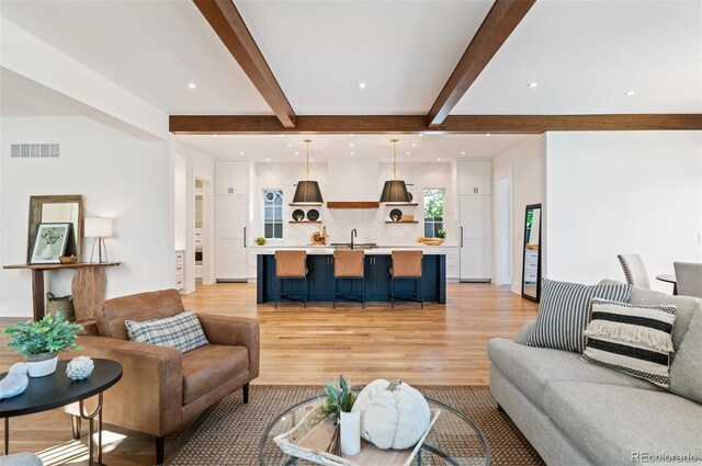 living room with light wood-type flooring, beamed ceiling, and sink