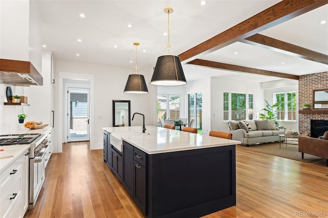 kitchen with sink, white cabinetry, hanging light fixtures, a fireplace, and a center island with sink