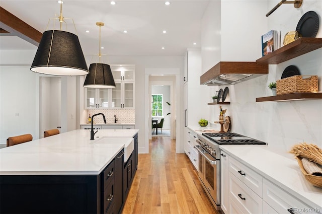 kitchen featuring pendant lighting, range with two ovens, a center island with sink, and light wood-type flooring