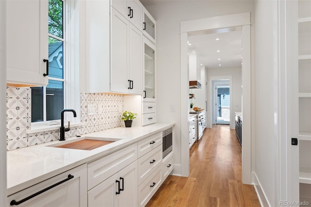 kitchen with decorative backsplash, white cabinetry, light hardwood / wood-style flooring, and light stone counters