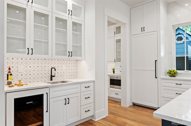 bar featuring white cabinetry, tasteful backsplash, beverage cooler, light hardwood / wood-style flooring, and sink