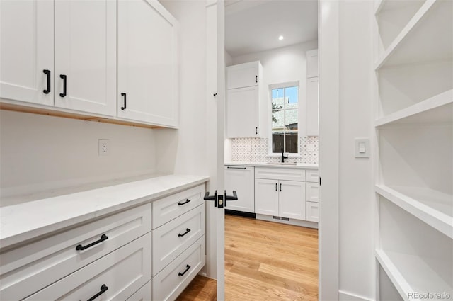 kitchen with dishwasher, sink, white cabinets, light hardwood / wood-style flooring, and backsplash