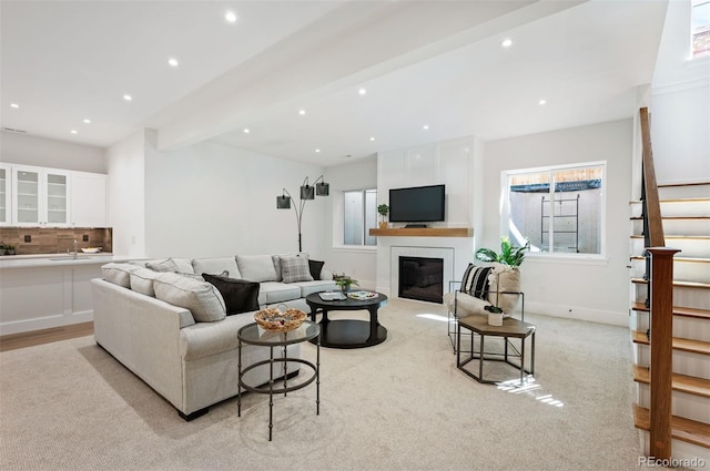 living room with beam ceiling, sink, and light colored carpet