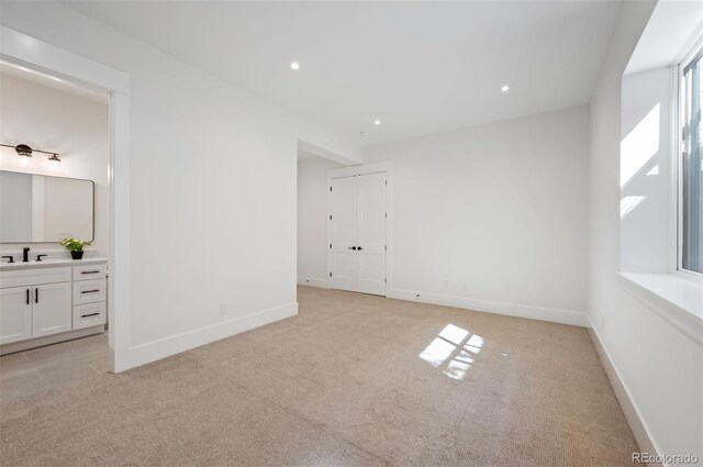 unfurnished bedroom featuring ensuite bath, light colored carpet, and sink