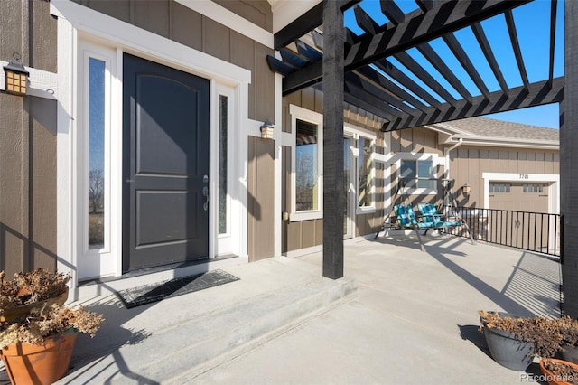 doorway to property with board and batten siding, a pergola, and a shingled roof