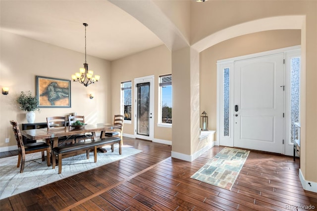 entryway with dark wood finished floors, a chandelier, arched walkways, and baseboards