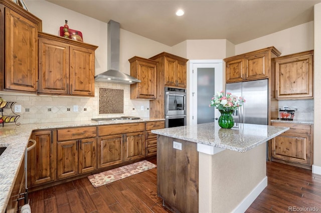 kitchen with brown cabinets, appliances with stainless steel finishes, wall chimney exhaust hood, and dark wood finished floors