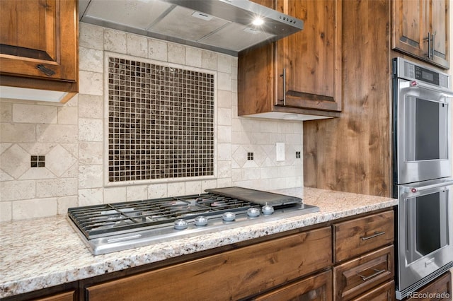 kitchen with light stone counters, decorative backsplash, appliances with stainless steel finishes, and wall chimney range hood