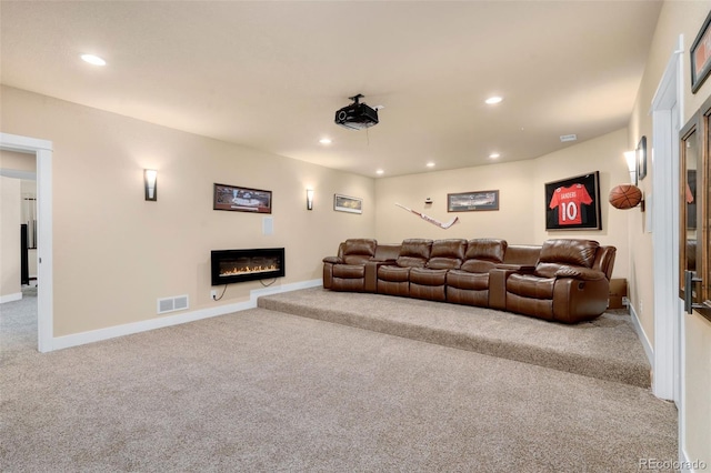 carpeted home theater room with a glass covered fireplace, recessed lighting, visible vents, and baseboards