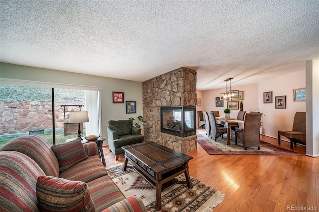 7815 Armadillo Trl, Evergreen, CO 80439 - living room with a notable chandelier, a stone fireplace, a textured ceiling, and light wood-style floors