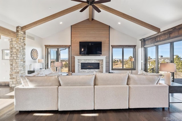 living room featuring ceiling fan, dark hardwood / wood-style floors, beamed ceiling, and a stone fireplace