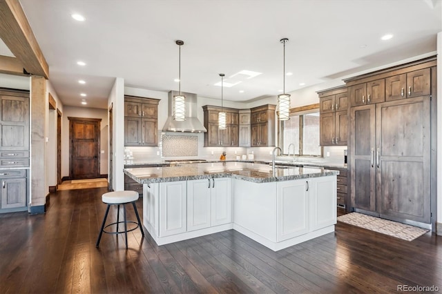 kitchen featuring decorative light fixtures, dark hardwood / wood-style flooring, light stone counters, wall chimney exhaust hood, and a large island