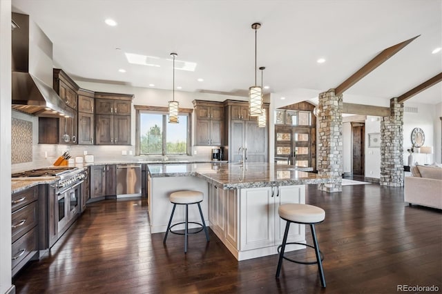 kitchen with a breakfast bar area, decorative columns, dark wood-type flooring, a large island, and wall chimney range hood