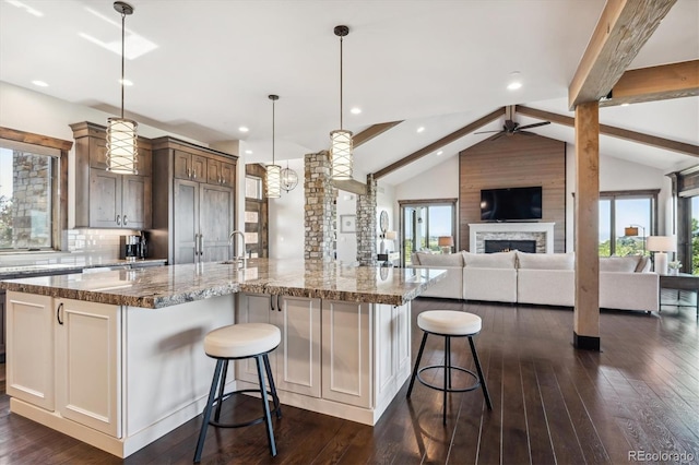 kitchen featuring a large island with sink, a kitchen bar, ceiling fan, hanging light fixtures, and lofted ceiling with beams