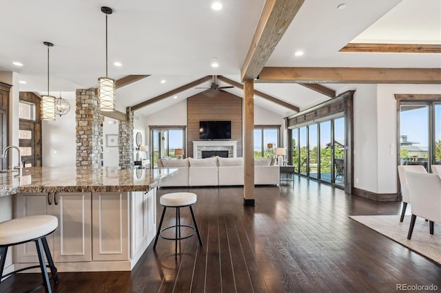 kitchen featuring ceiling fan with notable chandelier, light stone countertops, dark hardwood / wood-style floors, a kitchen breakfast bar, and pendant lighting