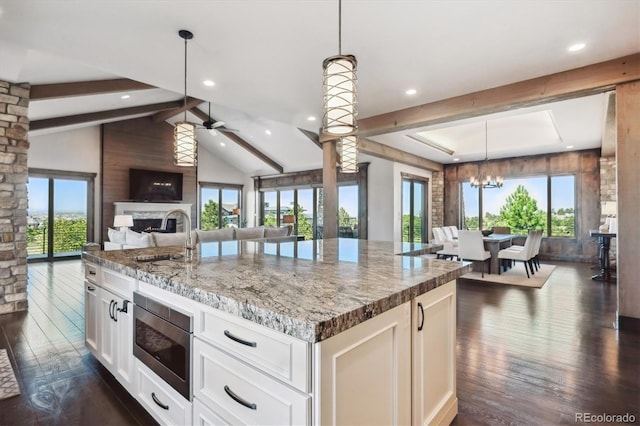 kitchen featuring light stone countertops, ceiling fan with notable chandelier, hanging light fixtures, and a kitchen island with sink