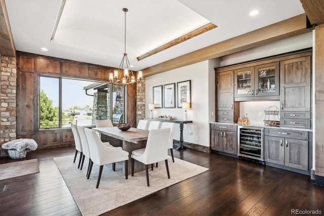 dining area with beverage cooler, a chandelier, dark wood-type flooring, and a raised ceiling