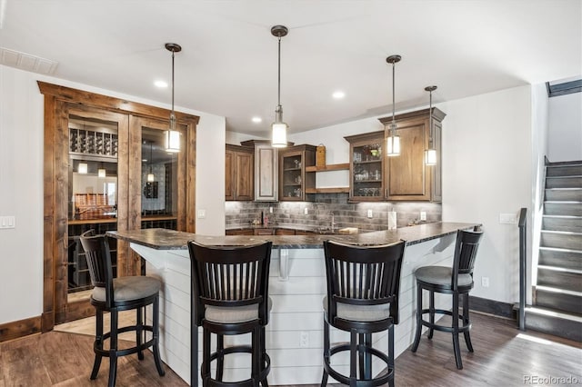 kitchen with dark stone countertops, pendant lighting, a kitchen breakfast bar, kitchen peninsula, and dark wood-type flooring