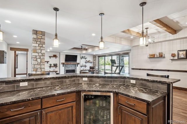 kitchen with light wood-type flooring, dark stone countertops, beamed ceiling, decorative light fixtures, and beverage cooler