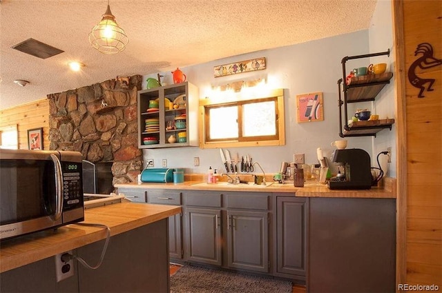 kitchen with a textured ceiling, pendant lighting, wooden counters, and gray cabinets