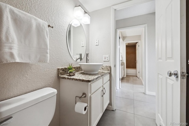 bathroom with toilet, tile patterned flooring, baseboards, vanity, and a textured wall