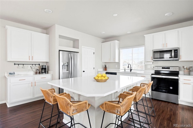 kitchen featuring a sink, appliances with stainless steel finishes, a breakfast bar, and dark wood finished floors