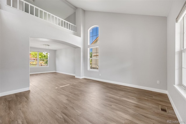 9147 W Rockland Pl, Littleton, CO 80128 - unfurnished living room featuring a chandelier, arched walkways, wood finished floors, and high vaulted ceiling