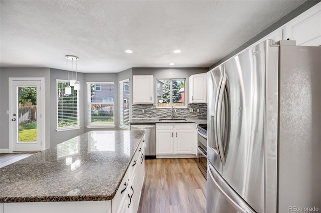 9147 W Rockland Pl, Littleton, CO 80128 - kitchen with stainless steel appliances, light wood-style flooring, white cabinets, a center island, and tasteful backsplash
