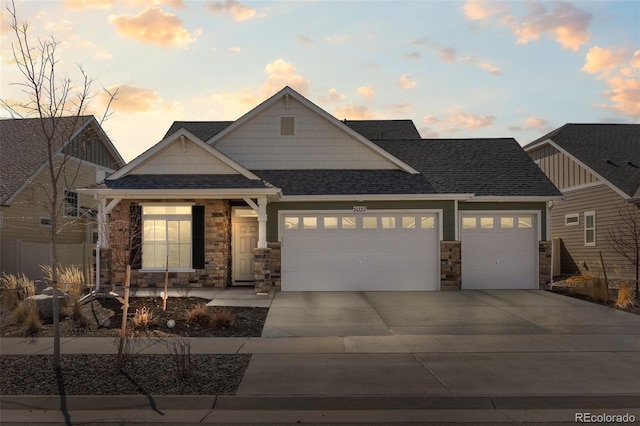 craftsman house with a garage, stone siding, driveway, and roof with shingles