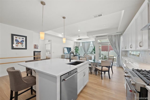 kitchen featuring visible vents, a kitchen island with sink, a sink, light wood-style floors, and appliances with stainless steel finishes