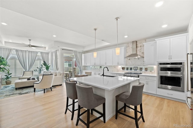 kitchen with wall chimney range hood, a breakfast bar, light countertops, stainless steel appliances, and a sink