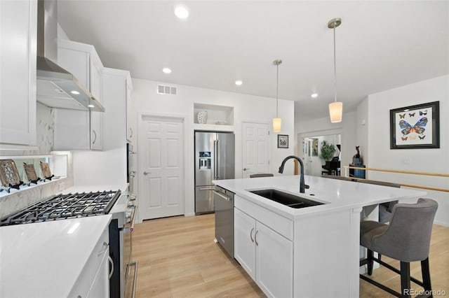 kitchen with visible vents, a sink, light wood-style floors, appliances with stainless steel finishes, and wall chimney range hood