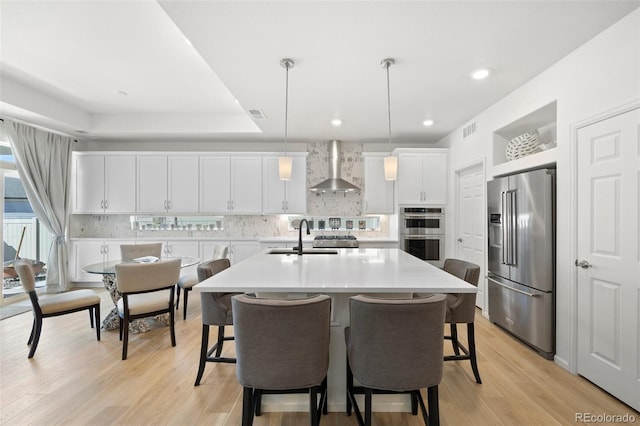 kitchen with visible vents, a kitchen bar, backsplash, appliances with stainless steel finishes, and wall chimney range hood