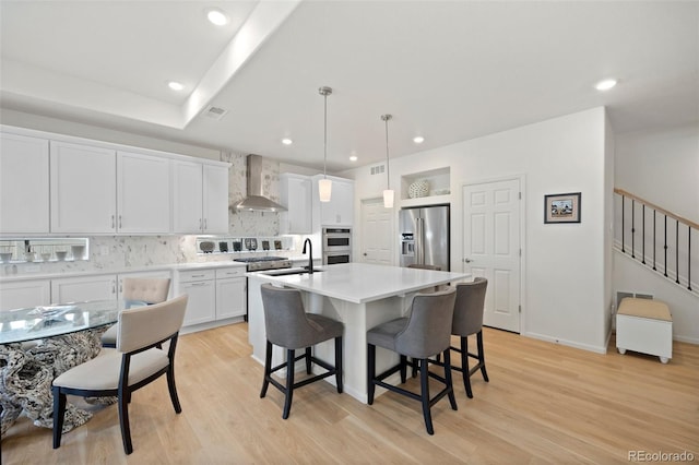 kitchen with a kitchen bar, light wood-style flooring, tasteful backsplash, stainless steel appliances, and wall chimney range hood